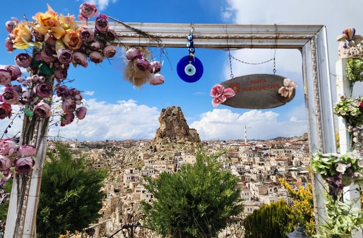 Çiçekli dekoratif çerçeve içinden görünen Ortahisar Kalesi ve taş evleriyle Kapadokya panoraması